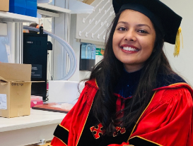 Divya Patel, sitting in a bioengineering lab with her University of Maryland graduation cap and gown.